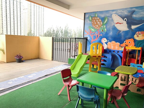 Un espace de jeux pour enfants avec un toboggan, des chaises colorées et une fresque représentant des créatures marines.