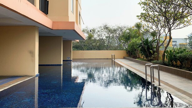 A swimming pool with a metal ladder, surrounded by a low wall and greenery. - Comfort Living 1Br Boutique Kemayoran Apartment (Jakarta)