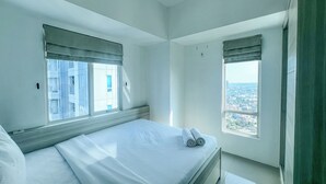 A bedroom with a bed, two windows, and a view of a cityscape.