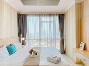 A hotel room with a large bed, a bedside table, a nightstand, a window with curtains, and a view of the city. - Good And Relaxing 2Br At Menteng Park Apartment (Jakarta)
