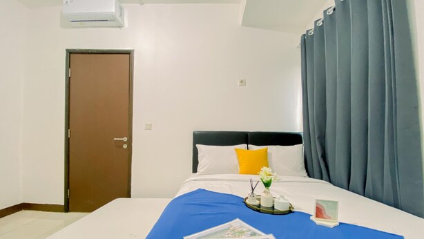 A hotel room with a bed, a window with curtains, a door, and an air conditioning unit. - Comfortable And Homey 1Br Boutique Kemayoran Apartment (Jakarta)
