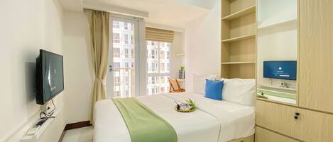 A hotel room with a bed, a TV, a desk, and a window with curtains.
