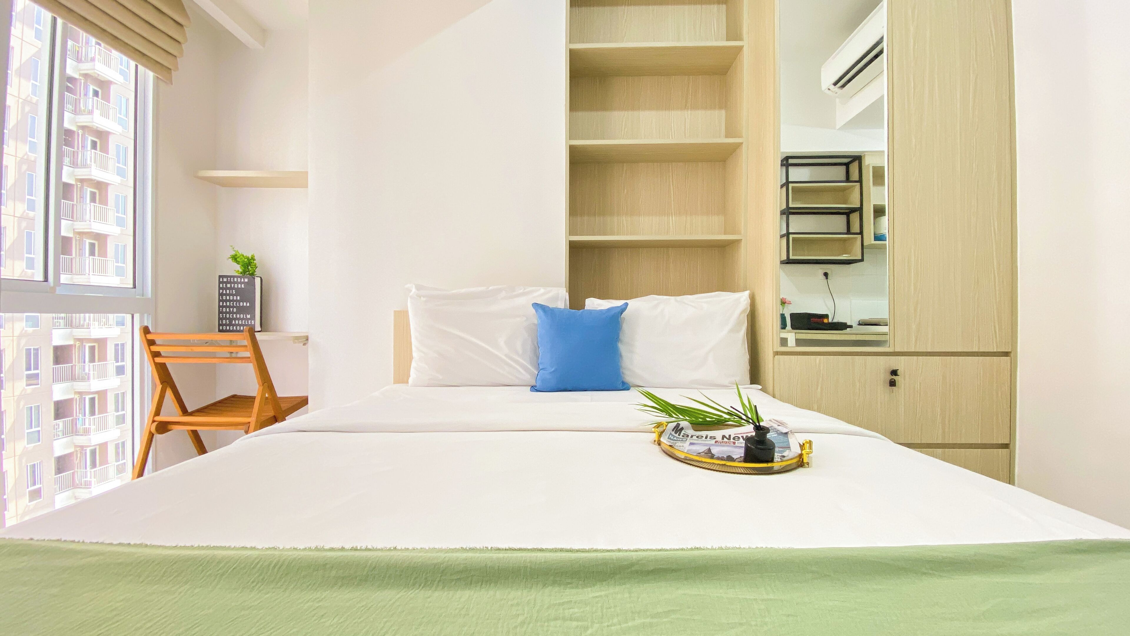 A neatly arranged hotel room with a bed, a chair, a small table with a plant, and a window with a view of a building.