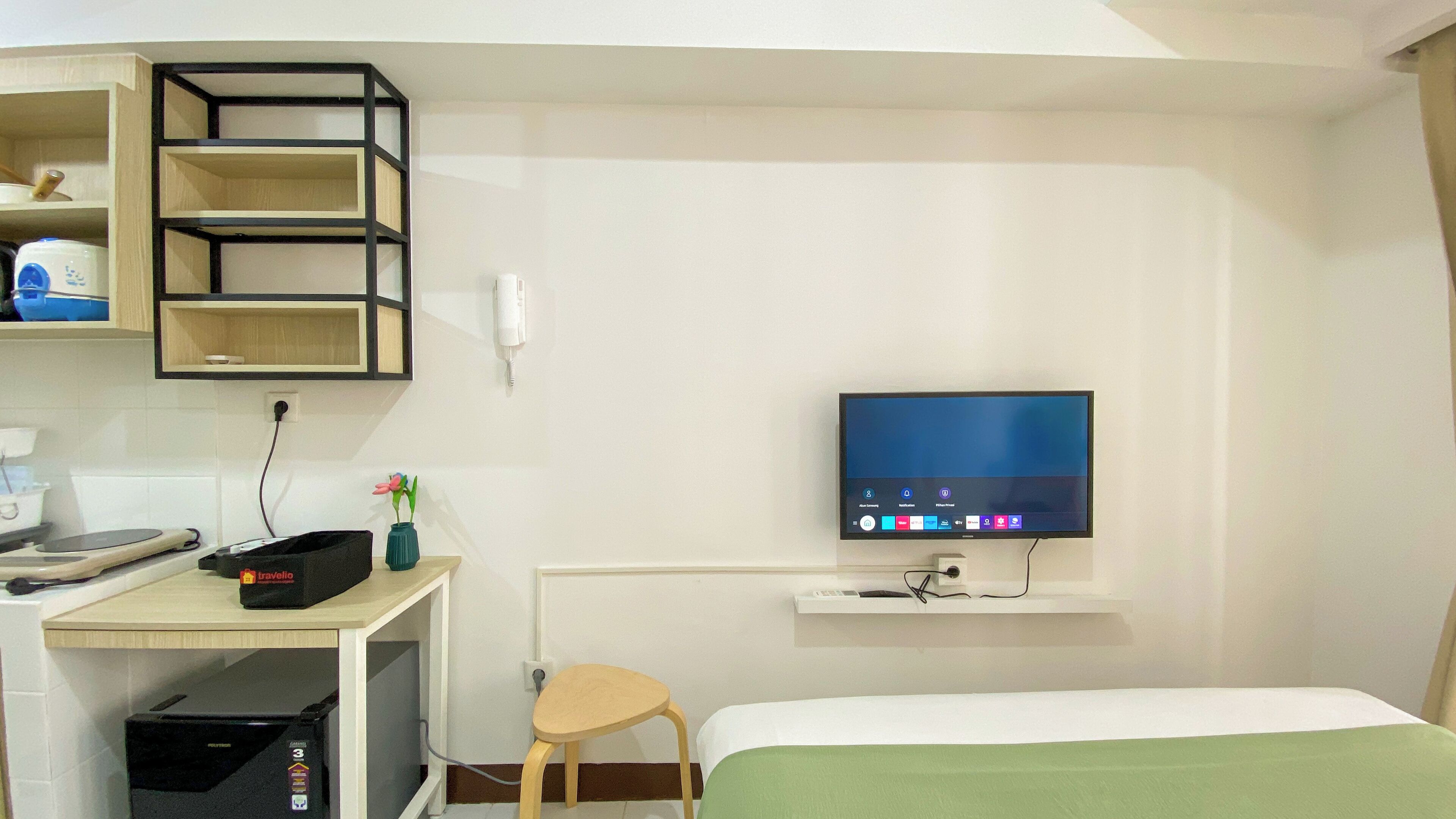 A hotel room with a bed, a desk with a computer, a TV mounted on the wall, and a small table.