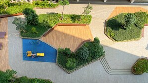 Vue aérienne d’un espace aménagé comprenant une aire de jeux bleue, des bancs en bois et diverses plantes vertes.