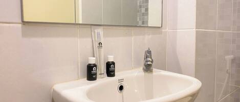 A bathroom sink with a mirror above it, a toothbrush holder, and two bottles of travel hygiene products.