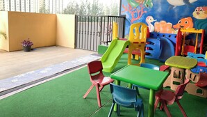 Een kinderspeelplaats met een glijbaan, kleurrijke stoelen en een muurschildering van zeedieren.