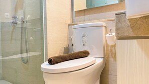 A bathroom with a toilet, shower enclosure, and towel storage.