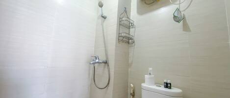 A bathroom with a shower, toilet, and a small shelf with toiletries.