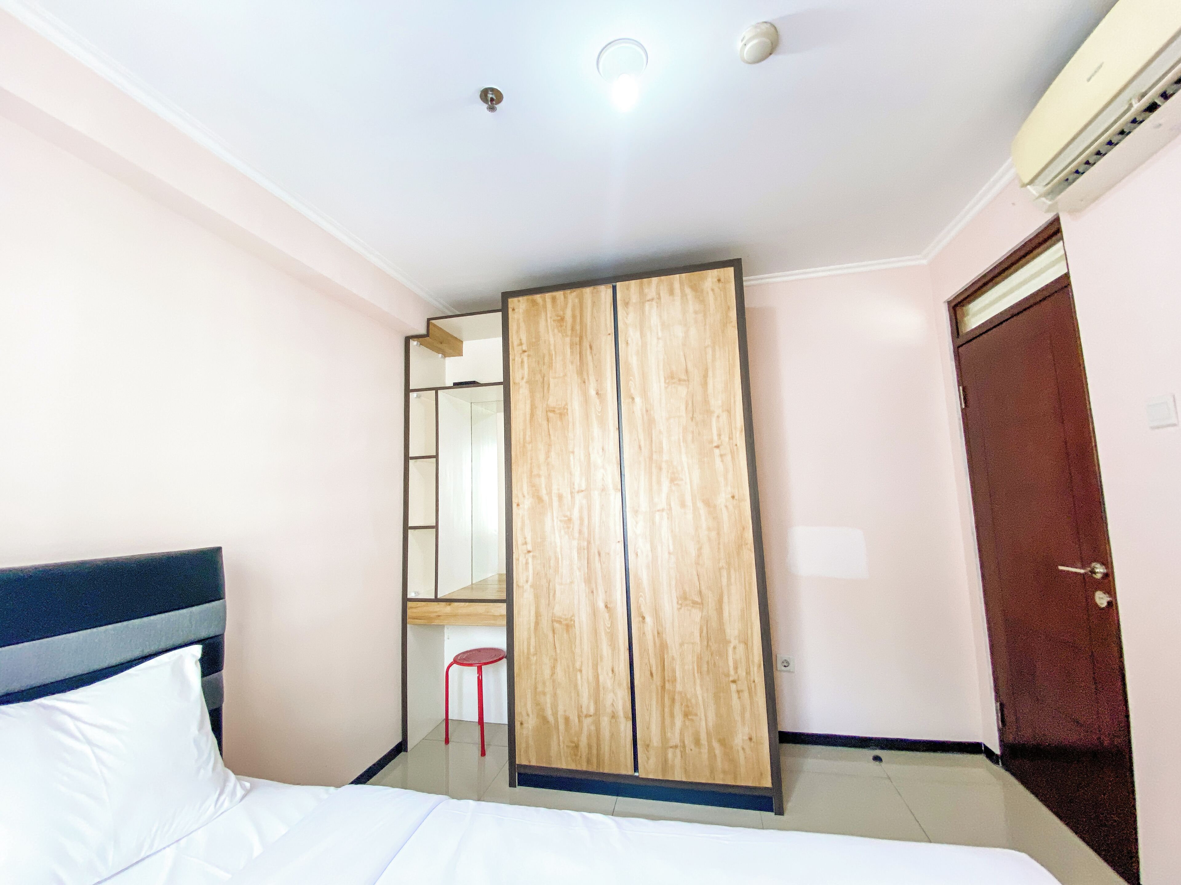 A hotel room with a bed, a wooden wardrobe, a red chair, a mirror, and a door.