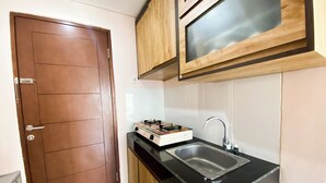 A compact kitchen with a brown door, a gas stove, a sink, and wooden cabinets. - Minimalist 2Br With Pool View At Gateway Pasteur Apartent (Cimahi)