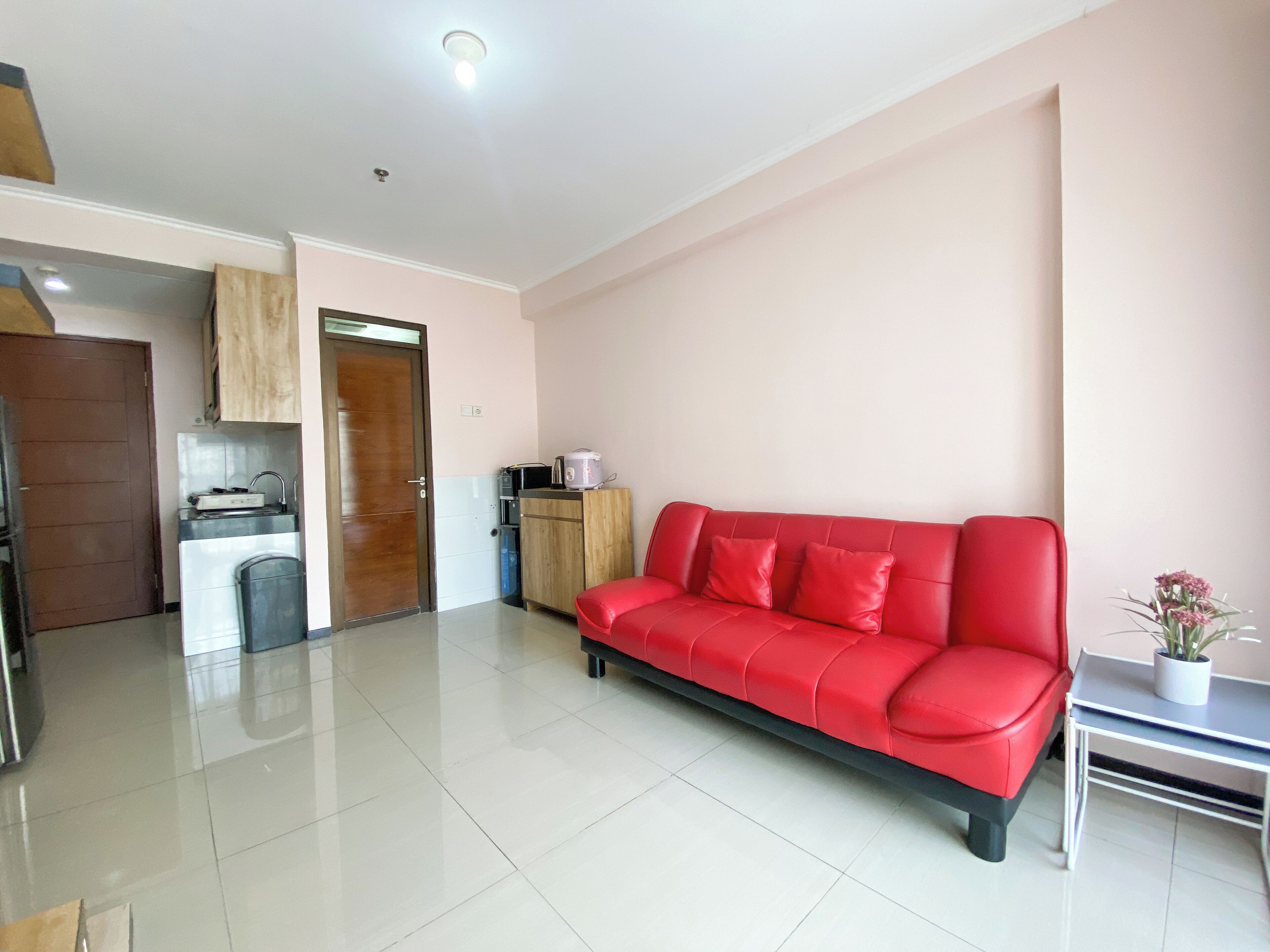 A modern living room with a red sofa, a small table, and a kitchen area with cabinets and appliances.