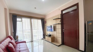 A living room with a red sofa, a TV on a wooden stand, a door, and a refrigerator. - Minimalist 2Br With Pool View At Gateway Pasteur Apartent (Cimahi)