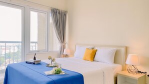 A hotel room with a large bed, a bedside table with a lamp, a window with curtains, and a view of the outside.