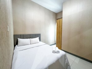 Una habitación de hotel con una cama grande, una puerta de madera y una pared sencilla.