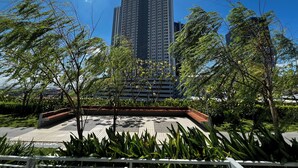 A high-rise building with a modern design, surrounded by lush greenery and a paved plaza.