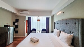 Quarto de hotel com uma cama grande, uma escrivaninha pequena, um frigorífico e uma janela com cortinas.