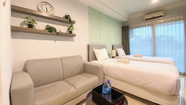 Een moderne hotelkamer met een bank, twee bedden, een klok en een kleine tafel met waterflessen.