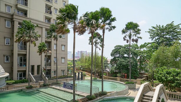 A swimming pool surrounded by palm trees and a multi-story building with balconies.