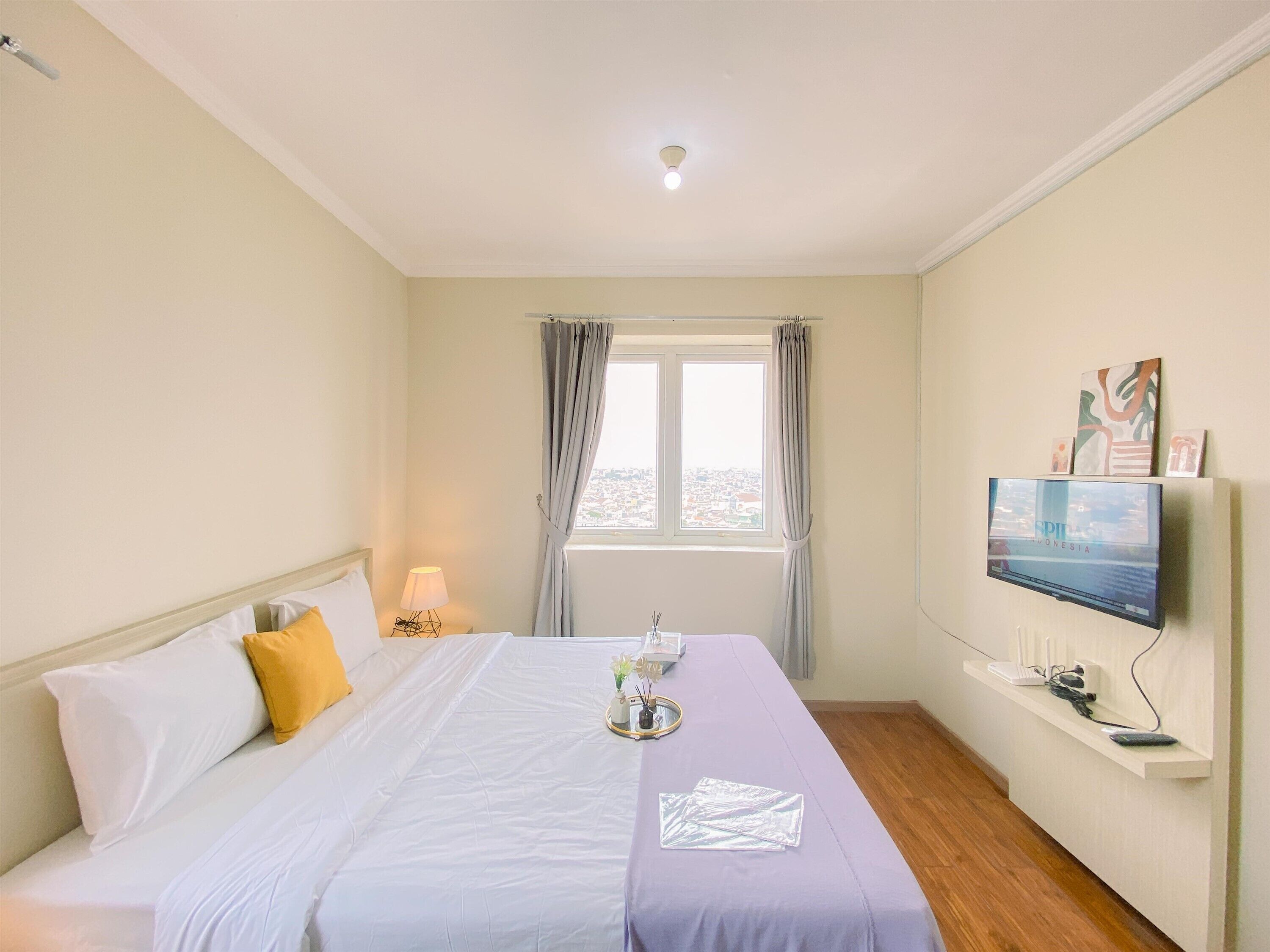 Habitación de hotel con cama, televisor, ventana con cortinas y vista a la ciudad.
