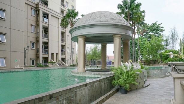 Un espace piscine agrémenté d’un kiosque, de palmiers et, au fond, d’un immeuble à plusieurs étages.