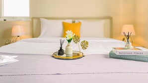 A neatly made bed with white and yellow pillows, a bedside table with a lamp, a tray with decorative items, and a book titled "Delicious Places Nordic Interiors Homes". - Best Location Studio At Grand Palace Kemayoran Apartment (Free Ipl & Utilities) (Jakarta)