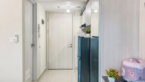 A hallway with a modern kitchen area, including a refrigerator, a coffee maker, and a potted plant. - Best Place And Restful Studio At Apartment Springlake Summarecon Bekasi (Bekasi)
