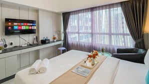 A hotel room with a bed, a desk with a flat-screen TV displaying various apps, a window with curtains, and a view of buildings outside. - Best Place And Restful Studio At Apartment Springlake Summarecon Bekasi (Bekasi)
