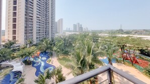 A high-rise building with a rooftop pool and a landscaped park area with palm trees and a playground. - Best Place And Wonderful 3Br Apartment Sky House Bsd Near Aeon Mall (Pagedangan)