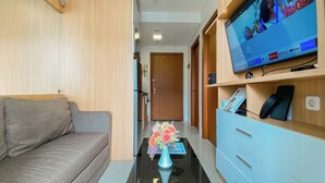 A modern living room with a sofa, a coffee table with a vase of flowers, and a TV on a wooden shelf. - Good Deal And Scenic 1Br Apartment At Woodland Park Residence (Jakarta)