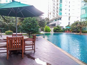 Un área junto a la piscina con muebles de madera y un parasol verde.