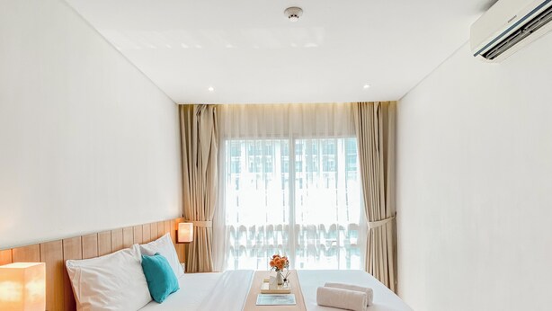 A hotel room with a large bed, a bedside table, a lamp, and a view of buildings through the window. - Good Deal And Scenic 1Br Apartment At Woodland Park Residence (Jakarta)