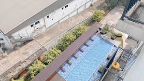 Vista aerea di un edificio con piscina sul tetto, circondato da alberi e da una grande struttura industriale.