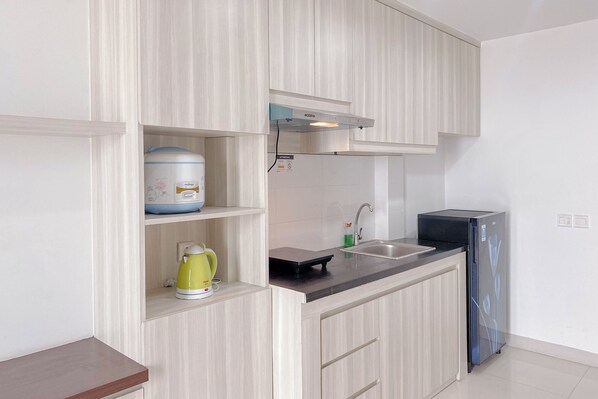 Une cuisine moderne avec des meubles de couleur bois clair, un évier en acier inoxydable, un réfrigérateur noir et une bouilloire posée sur le plan de travail.