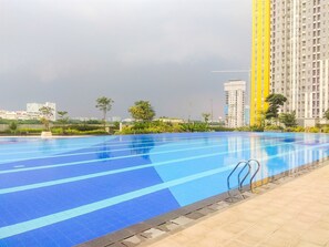 A swimming pool with blue lanes, surrounded by a tiled deck and greenery. - Restful And Minimalist Studio Springlake Summarecon Bekasi Apartment (Bekasi)
