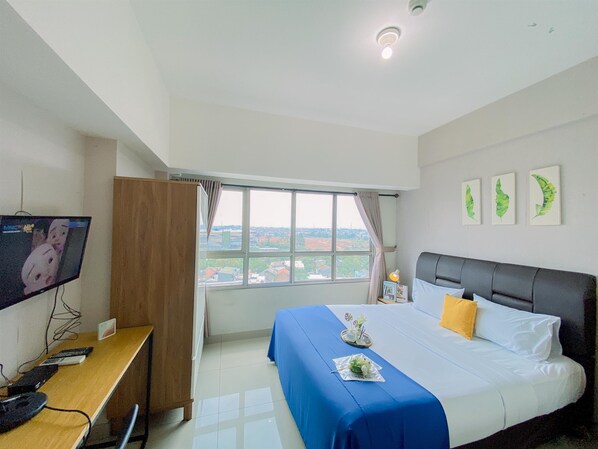A hotel room with a bed, a desk, a television, a window with a view, and three wall-mounted pictures. - Restful And Minimalist Studio Springlake Summarecon Bekasi Apartment (Bekasi)