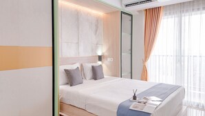 A modern hotel room with a large bed, a bedside table with a lamp, and a window with curtains.
