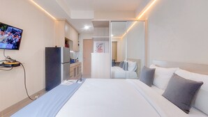 Una habitación de hotel con una cama, televisión, refrigerador y espejo.