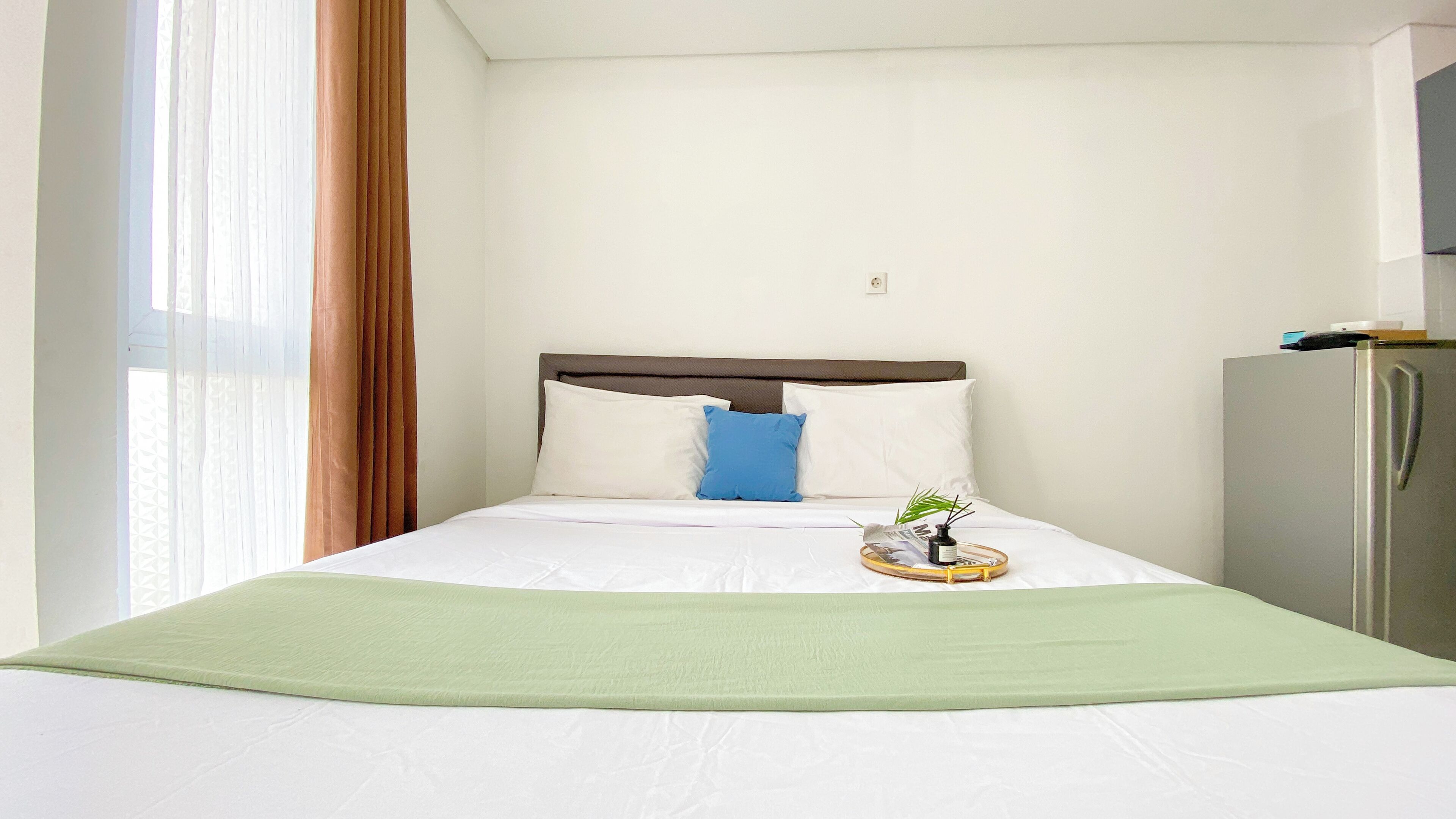 A hotel room with a bed, a nightstand, a refrigerator, and a window with curtains.