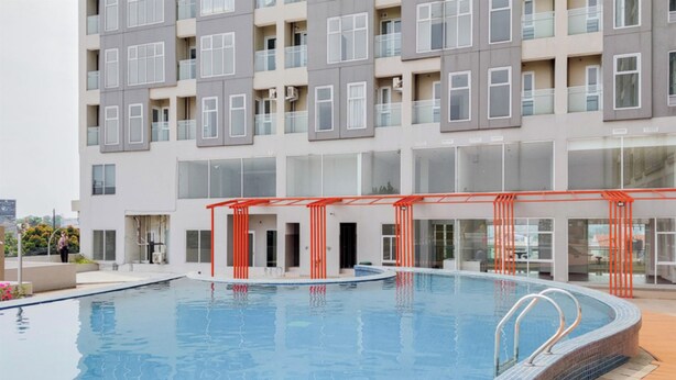 A modern building with a swimming pool, featuring a glass facade and a red structure near the pool. - Best Deal And Restful Studio At Amazana Serpong Apartment (South Tangerang)