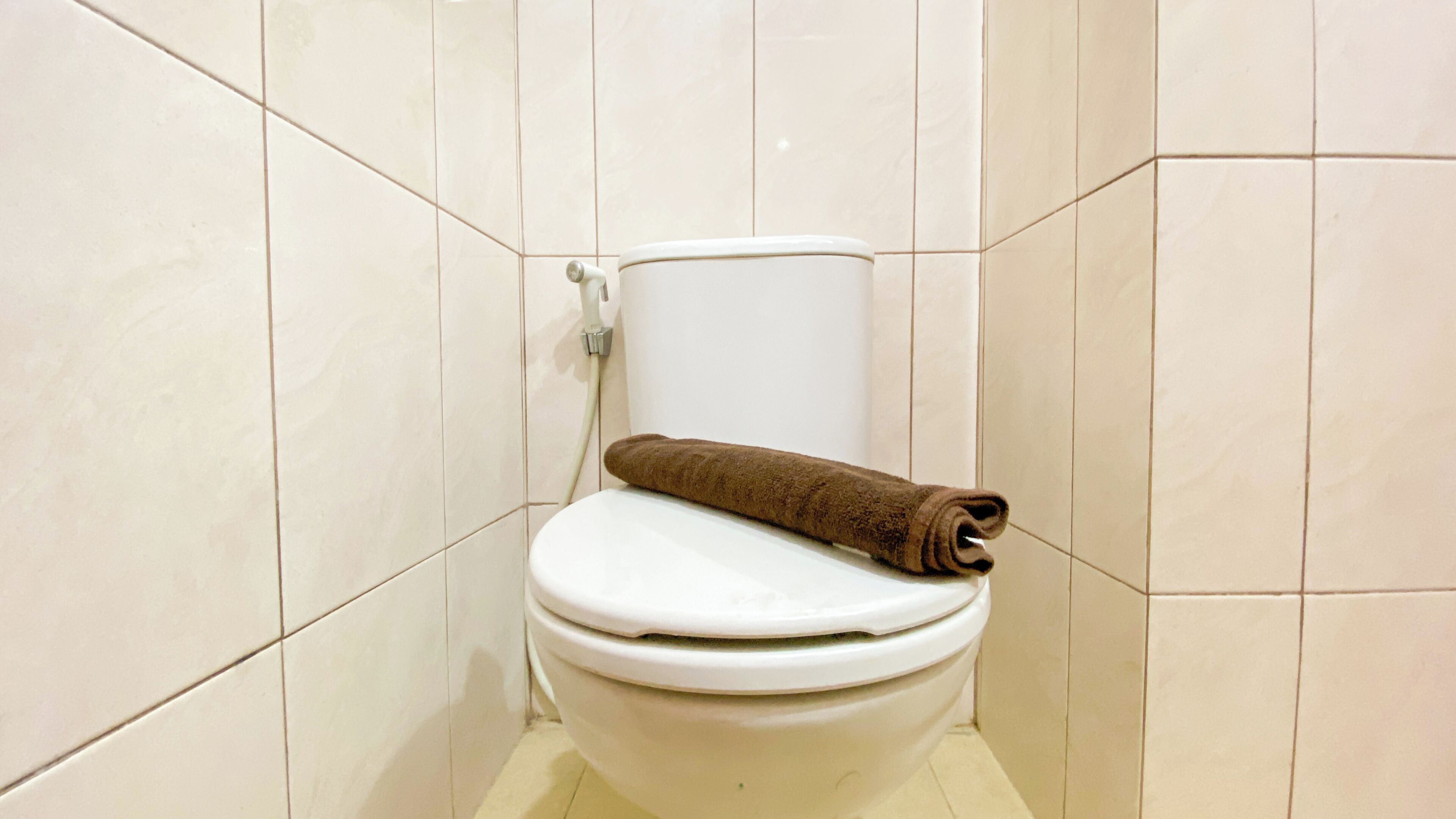 A toilet with a brown towel on the seat in a tiled bathroom.