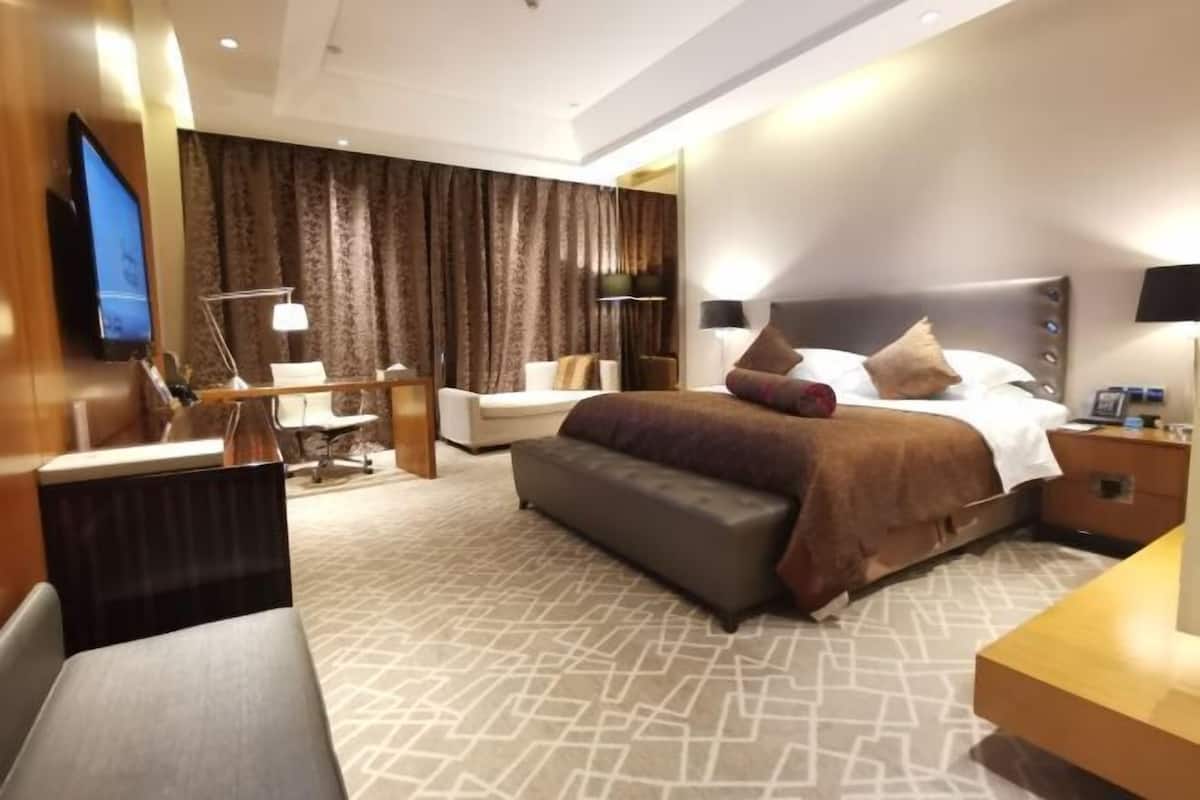 Ein modernes Hotelzimmer mit einem großen Bett, einem Schreibtisch, einem Stuhl und einem Fernseher.