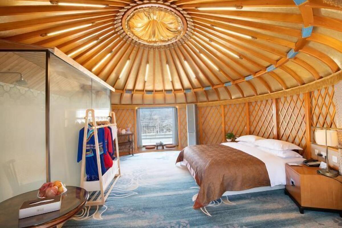 Ein yurt-ähnliches Zimmer mit Bett, Nachttisch und Blick ins Freie.