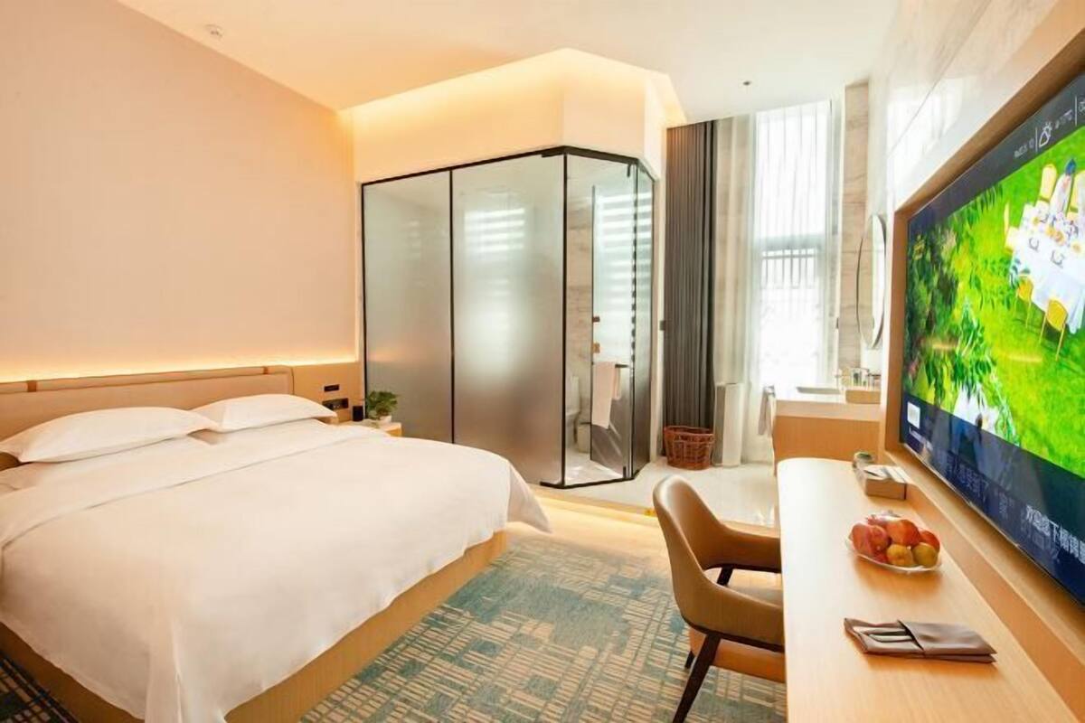 Ein Hotelzimmer mit Bett, Schreibtisch, Fernseher und einer Glastrennwand.