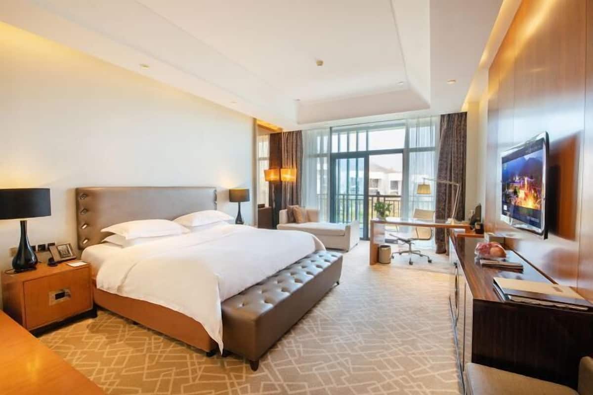 Ein Hotelzimmer mit einem großen Bett, einem Schreibtisch, einem Sessel und einem Fernseher.
