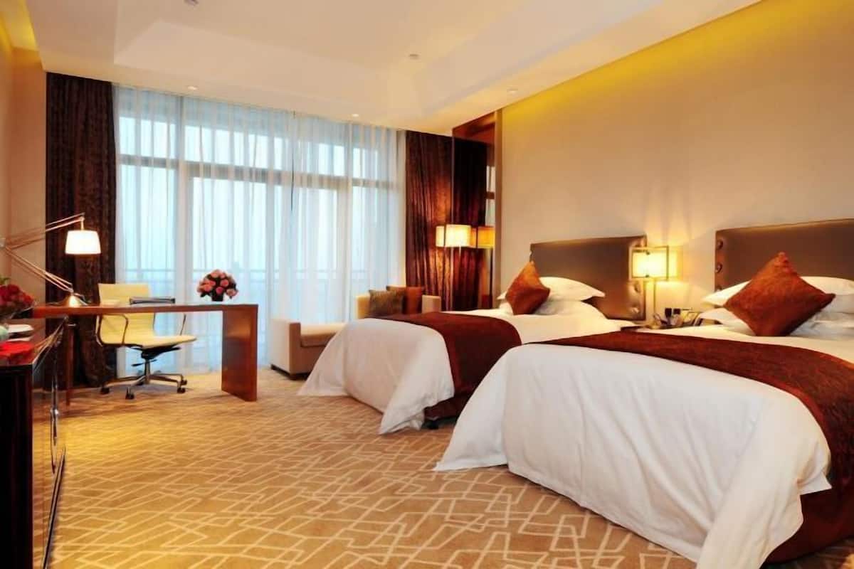 Ein Hotelzimmer mit zwei Betten, einem Schreibtisch, einem Stuhl und einem großen Fenster mit Vorhängen.