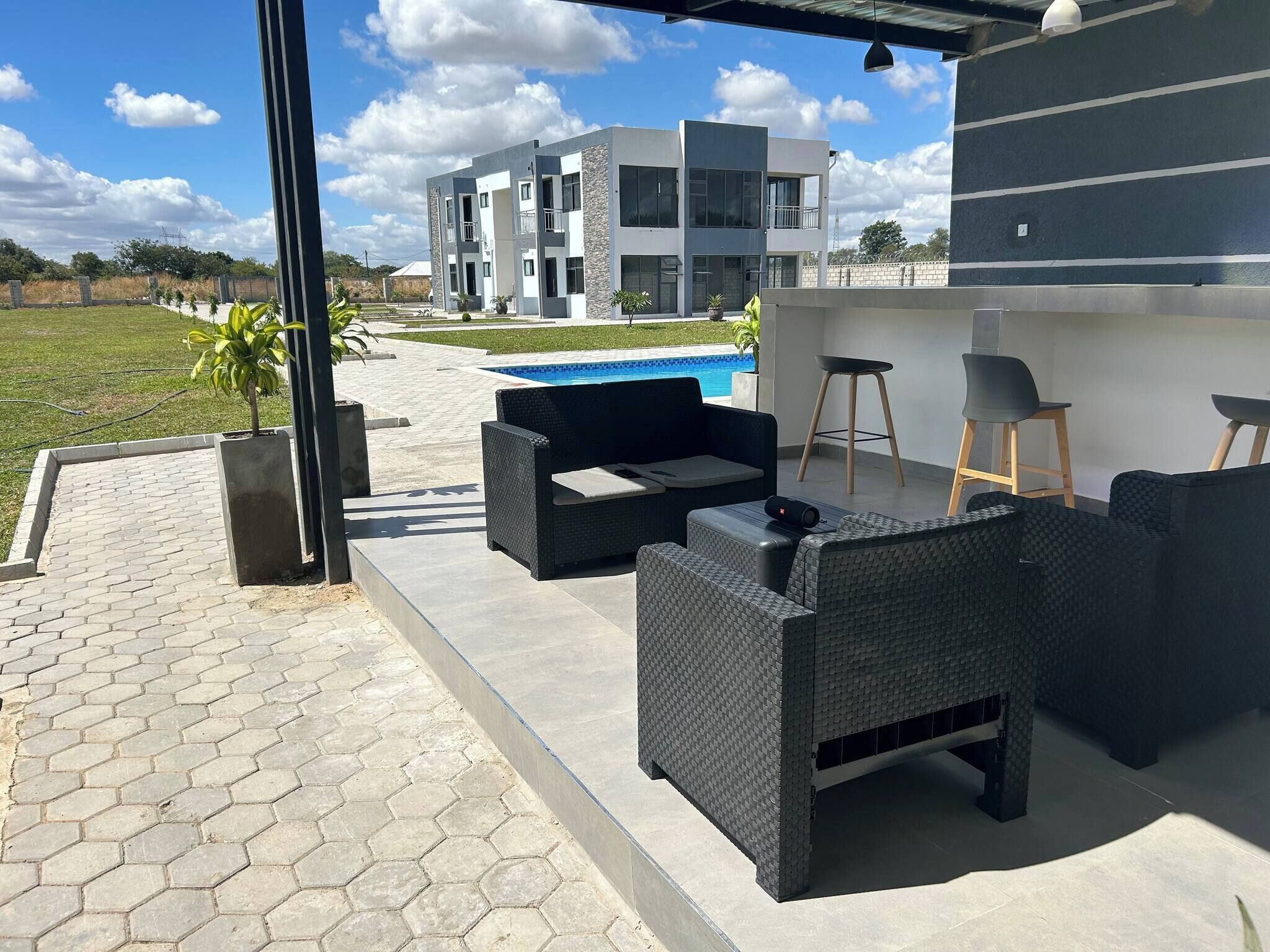 Une terrasse extérieure moderne, dotée de meubles en osier, d’une piscine et offrant une vue sur un bâtiment contemporain.