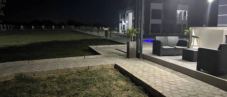 Een terras met honingraatbestrating, een gazon en een gebouw met een modern ontwerp op de achtergrond.