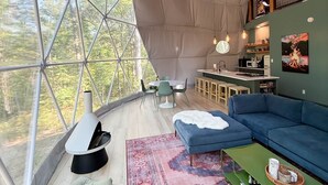 Une tente spacieuse comprenant un coin repas, une cuisine et un espace salon avec vue sur la forêt.