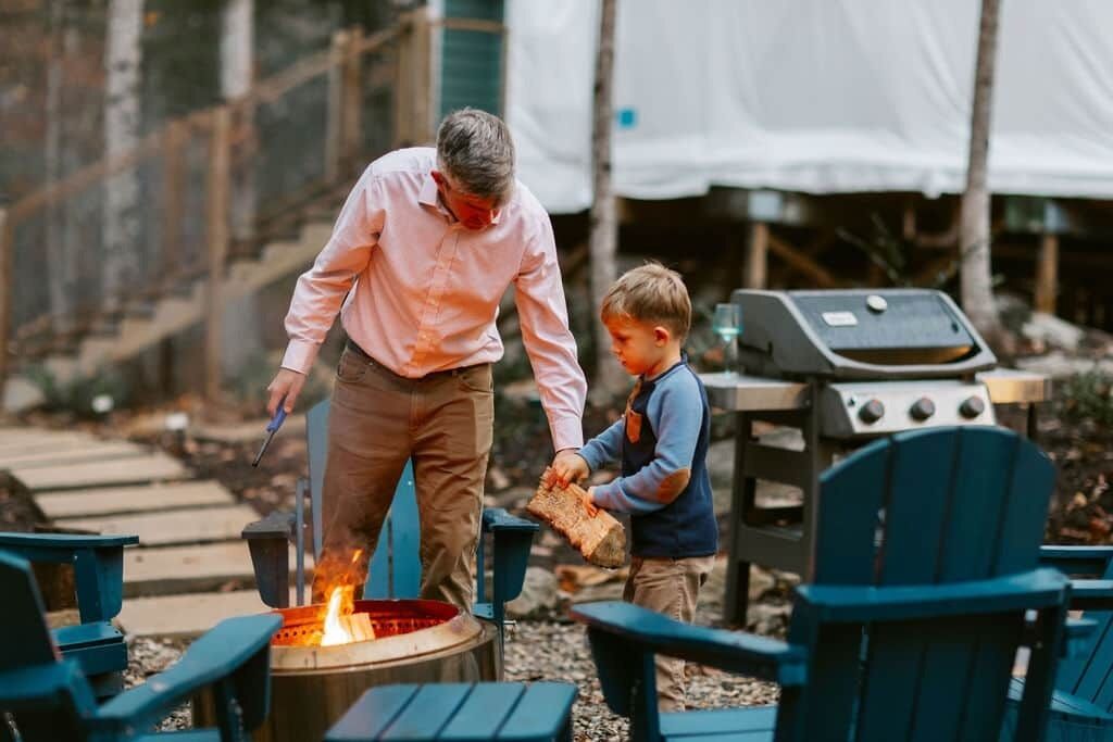 Een man en een kind bij een vuurkuil met een barbecue in een achtertuin.